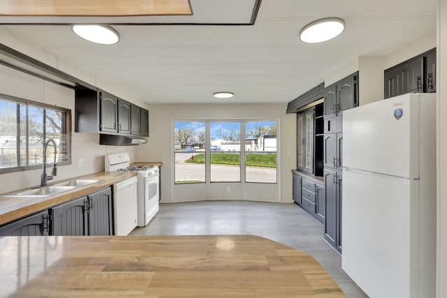 kitchen with a sink, light wood-style floors, wood counters, under cabinet range hood, and white appliances