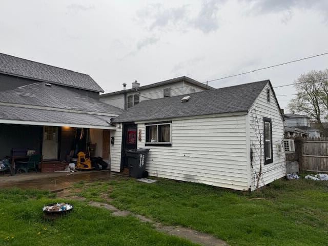 rear view of house featuring a lawn, roof with shingles, fence, and a patio