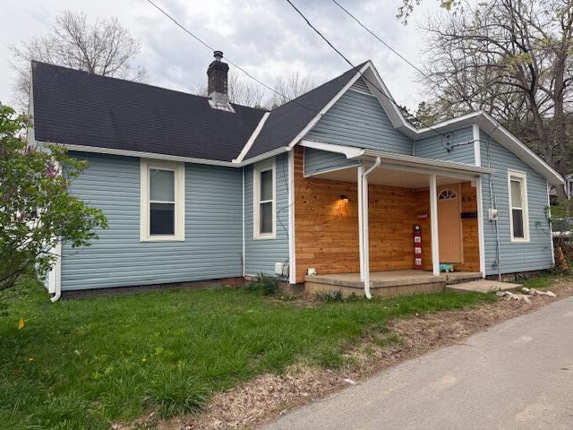 view of front of house with a porch, a chimney, and a front yard