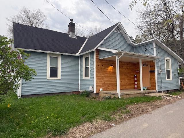 view of front of house with covered porch, a chimney, and a front lawn