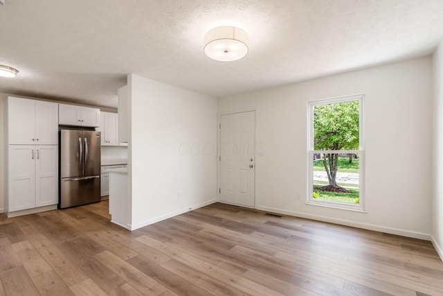 unfurnished dining area with visible vents, a textured ceiling, light wood finished floors, and baseboards