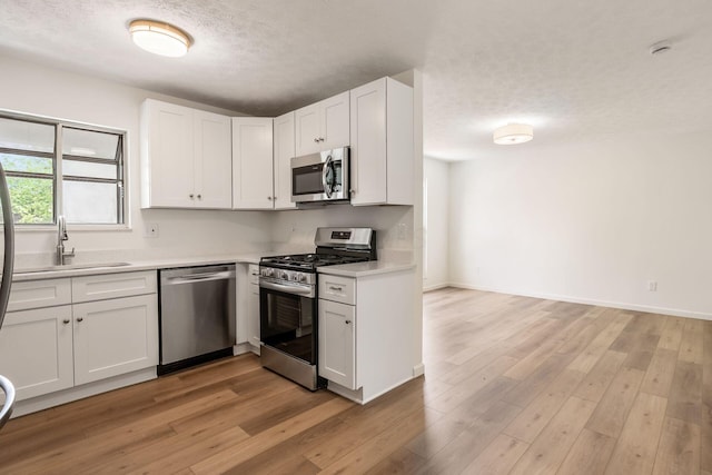 kitchen with appliances with stainless steel finishes, a sink, light countertops, a textured ceiling, and white cabinetry