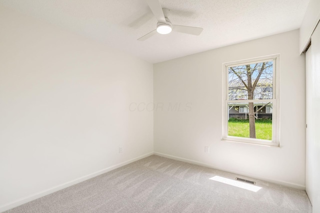 carpeted empty room featuring visible vents, a ceiling fan, and baseboards