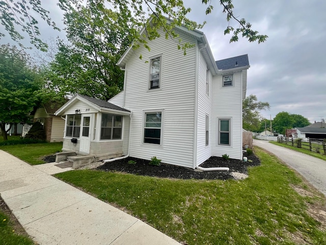 view of side of property featuring a lawn, fence, and a sunroom