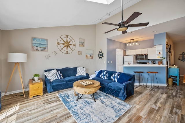 living area with ceiling fan, rail lighting, light wood-style flooring, baseboards, and a skylight