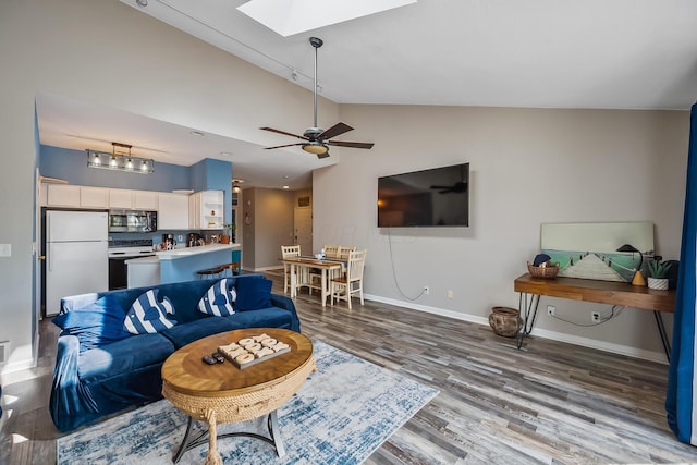 living room featuring vaulted ceiling with skylight, baseboards, a ceiling fan, and wood finished floors