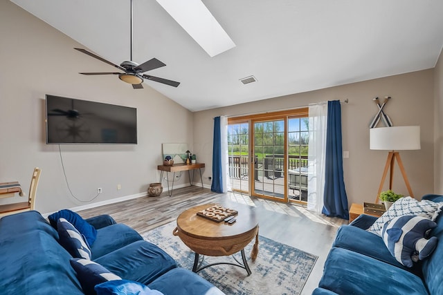 living area with vaulted ceiling with skylight, a ceiling fan, visible vents, wood finished floors, and baseboards