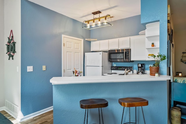 kitchen with visible vents, stainless steel microwave, freestanding refrigerator, a peninsula, and dark wood-type flooring