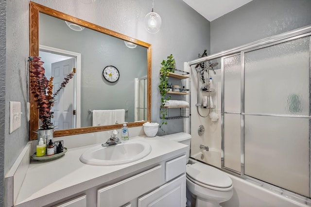 bathroom featuring vanity, a textured wall, enclosed tub / shower combo, and toilet