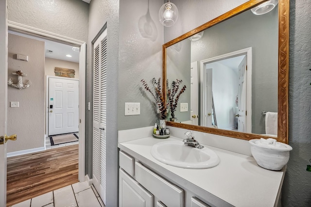 bathroom with a textured wall, baseboards, tile patterned flooring, and vanity