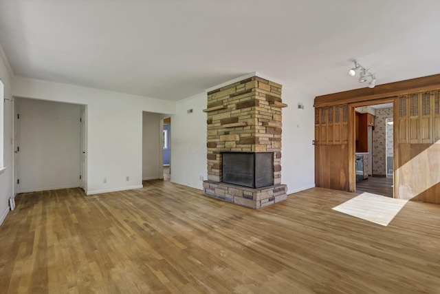 unfurnished living room with baseboards, track lighting, wood finished floors, and a fireplace