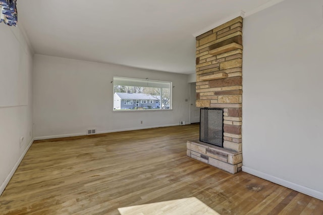 unfurnished living room with baseboards, visible vents, a stone fireplace, and wood finished floors