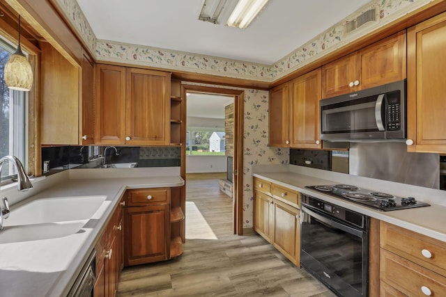 kitchen with wallpapered walls, a sink, black appliances, and light wood-type flooring