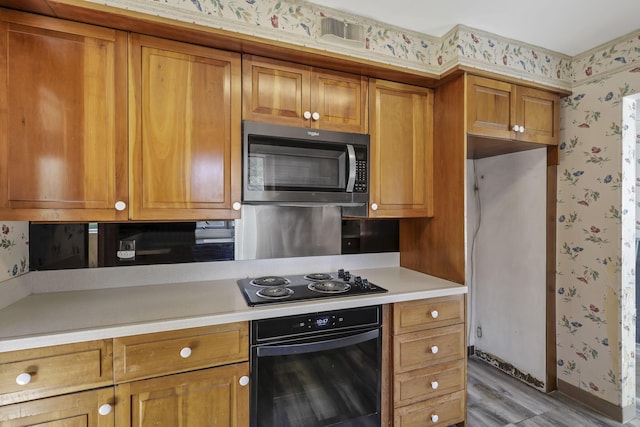 kitchen featuring light countertops, wallpapered walls, brown cabinetry, and black appliances