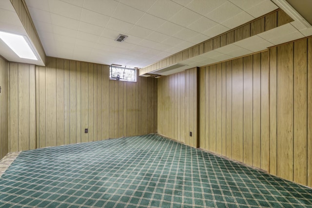 basement with carpet flooring, wood walls, and visible vents