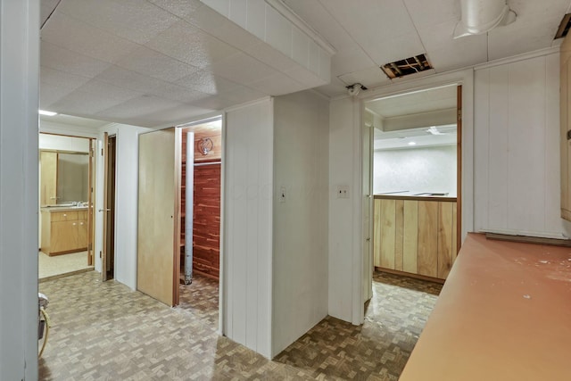 hallway featuring a paneled ceiling and wooden walls