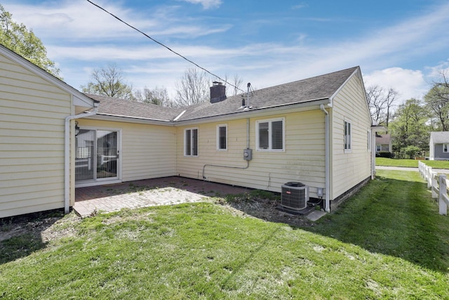 back of property featuring a chimney, a patio area, central air condition unit, a yard, and a shingled roof
