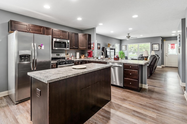 kitchen featuring dark brown cabinetry, a kitchen island, appliances with stainless steel finishes, light wood-type flooring, and a peninsula