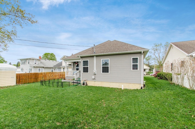 rear view of house with a lawn, fence, and a shingled roof
