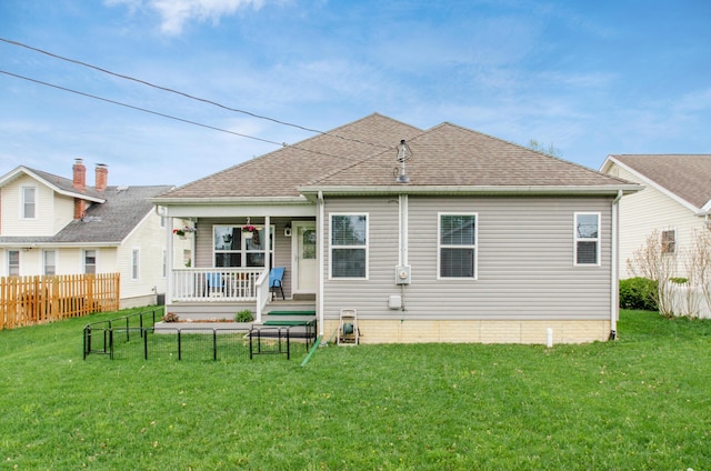 back of house with covered porch, a lawn, fence, and a shingled roof