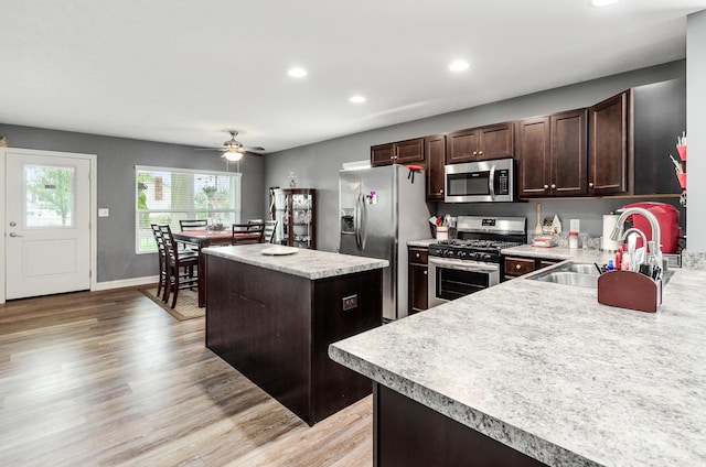 kitchen featuring light wood-style floors, appliances with stainless steel finishes, a sink, and a center island