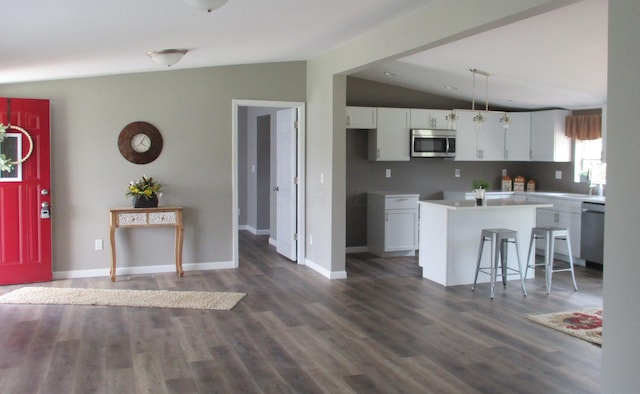 kitchen with white cabinets, dark wood-style flooring, stainless steel appliances, lofted ceiling, and a kitchen island