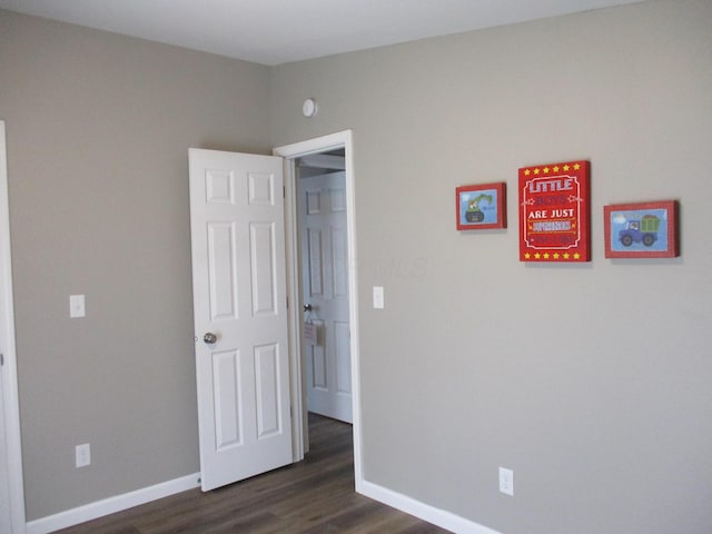 unfurnished bedroom with baseboards and dark wood-style floors