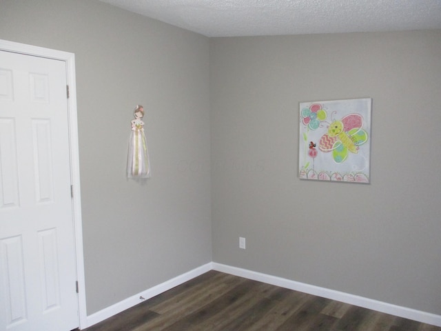 spare room with a textured ceiling, baseboards, and dark wood-style floors