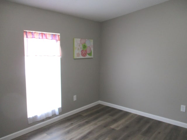 unfurnished room with baseboards and dark wood-style floors