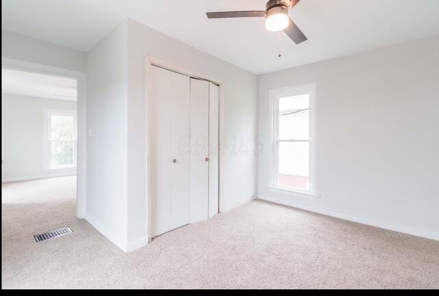 unfurnished bedroom featuring a closet, a ceiling fan, visible vents, baseboards, and carpet flooring