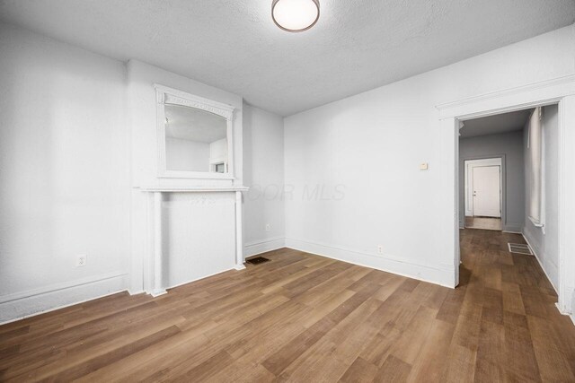 unfurnished living room featuring visible vents, baseboards, a textured ceiling, and wood finished floors