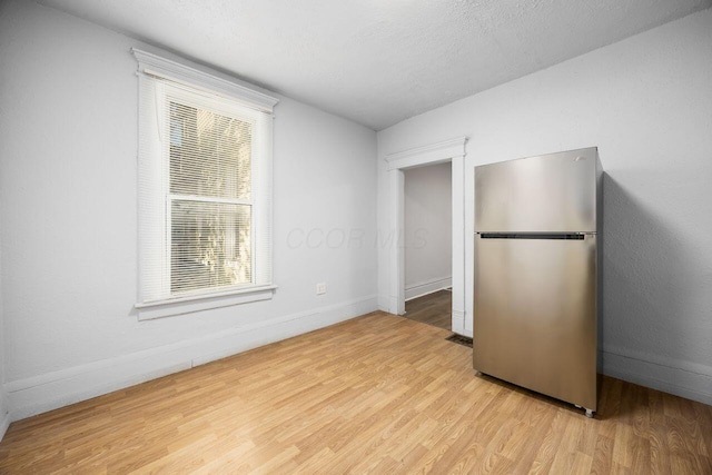 unfurnished bedroom with light wood-style floors, baseboards, multiple windows, and freestanding refrigerator