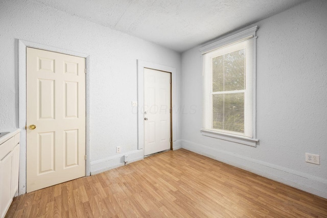 unfurnished bedroom with baseboards, light wood-type flooring, and a textured ceiling
