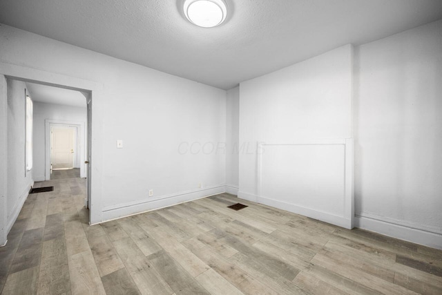 unfurnished room with visible vents, a textured ceiling, baseboards, and wood finished floors