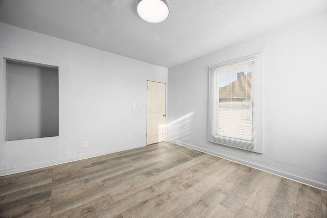 unfurnished room featuring baseboards, a textured ceiling, and wood finished floors