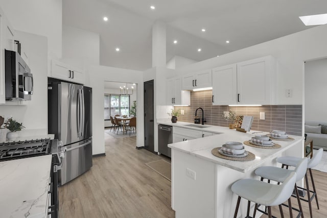 845 Mcnaughten Rd, Columbus, OH 43213 - kitchen featuring a sink, white cabinets, a peninsula, stainless steel appliances, and light wood-style flooring