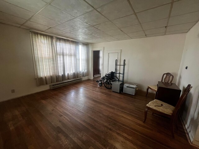 interior space with a baseboard radiator, a drop ceiling, and wood finished floors