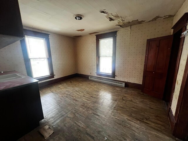 interior space featuring multiple windows, a baseboard heating unit, wallpapered walls, and wood finished floors