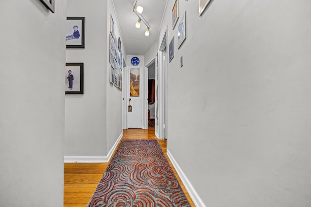 hallway featuring track lighting, baseboards, and wood finished floors