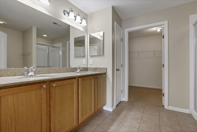 bathroom with double vanity, a stall shower, a sink, tile patterned floors, and baseboards