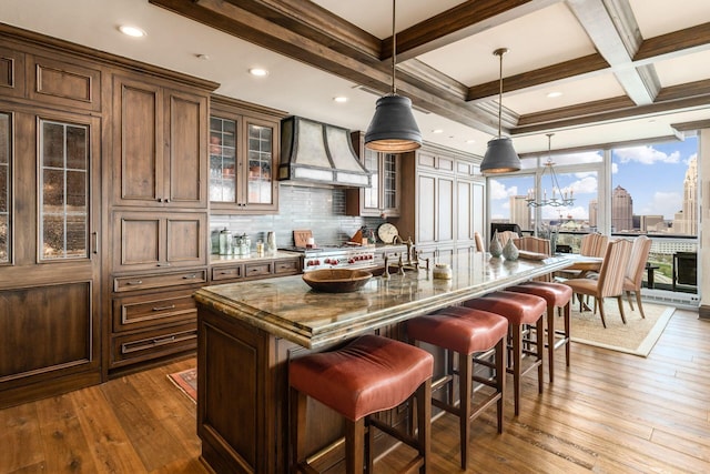 kitchen featuring a breakfast bar area, dark wood-style floors, custom exhaust hood, and dark stone counters