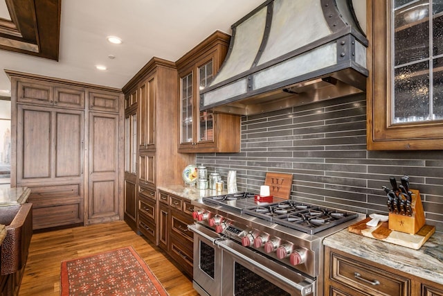 kitchen with recessed lighting, tasteful backsplash, custom range hood, range with two ovens, and light wood finished floors