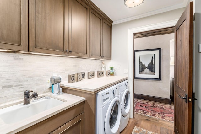 laundry room featuring ornamental molding, wood finished floors, washing machine and clothes dryer, a sink, and cabinet space