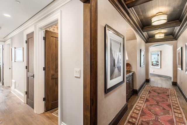 hall featuring arched walkways, ornamental molding, baseboards, and light wood finished floors