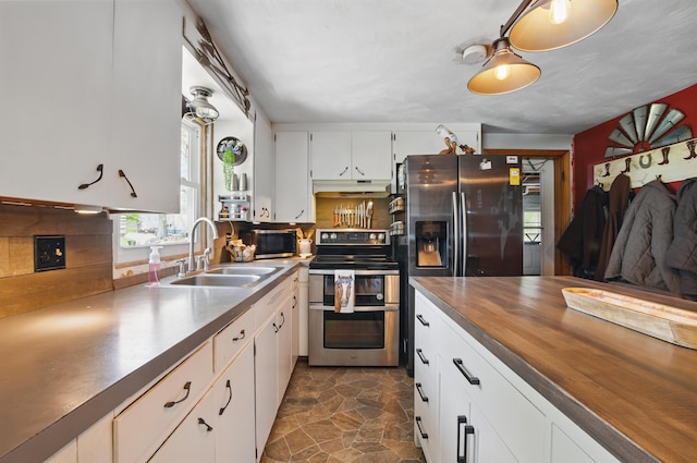 kitchen featuring butcher block counters, under cabinet range hood, white cabinets, a sink, and stainless steel appliances