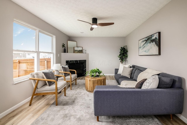 3141 Amberfield Dr, Columbus, OH 43232 - living area with a premium fireplace, a textured ceiling, light wood-style flooring, a ceiling fan, and baseboards