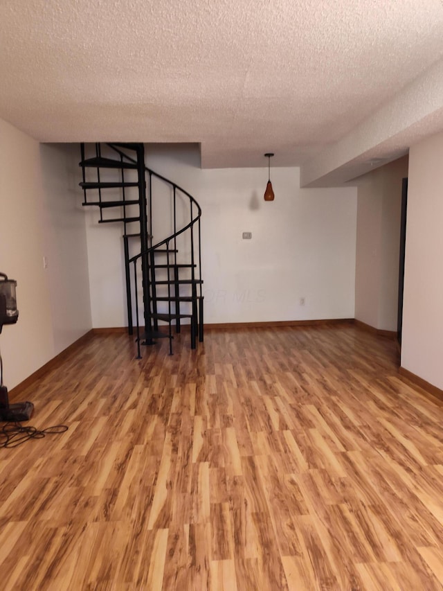 unfurnished living room featuring stairway, baseboards, light wood finished floors, and a textured ceiling