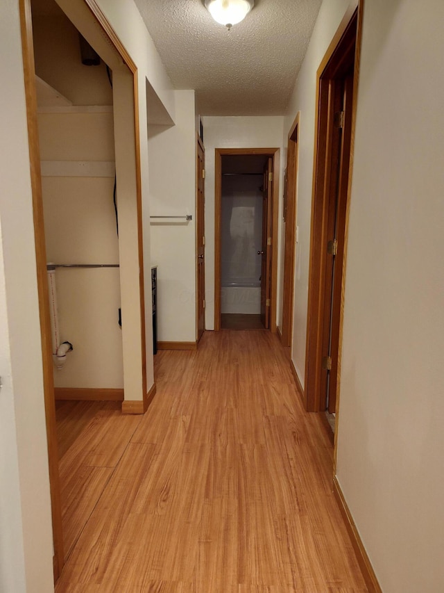 hall featuring baseboards, light wood finished floors, and a textured ceiling