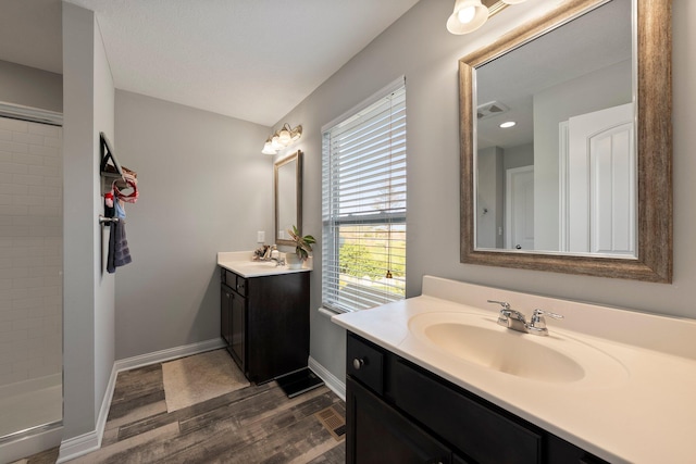 bathroom with wood finished floors, baseboards, two vanities, a sink, and a stall shower