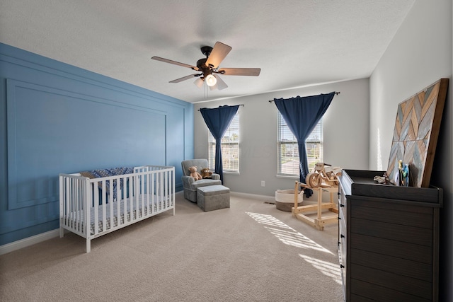 carpeted bedroom with a nursery area, baseboards, a ceiling fan, and a textured ceiling